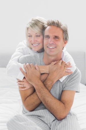 Embracing couple smiling at camera at home in bedroomの写真素材