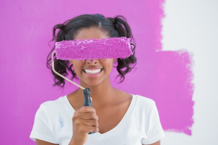 Pretty woman holding paintroller over her face against a pink wallの写真素材