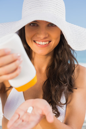 Smiling young brunette on the beach taking care of her body putting on sun creamの写真素材