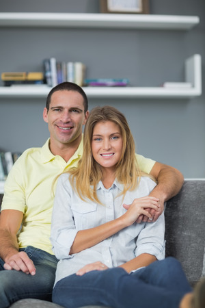 Smiling couple sitting on their couch in living room at homeの写真素材