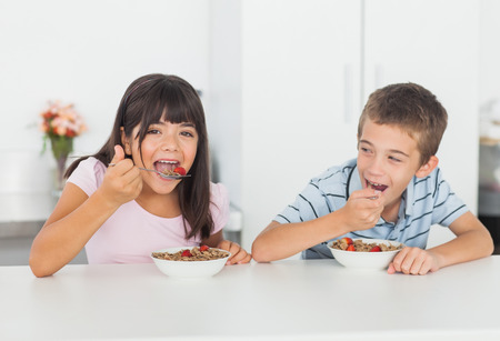 Siblings eating cereal for breakfast in kitchen at homeの写真素材