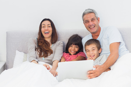 Happy family lying in bed using their laptop at home