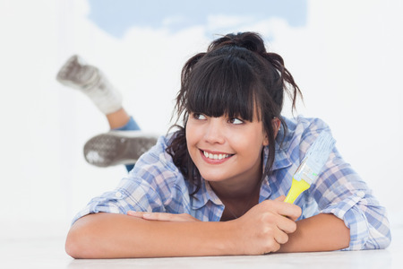 Smiling woman lying on floor holding paint brush looking upの写真素材