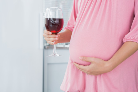 Expecting woman in her kitchen with red wine in right handの写真素材