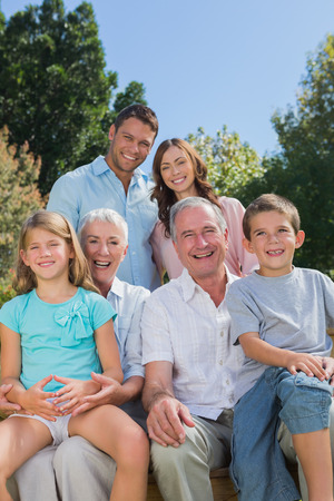 Cheerful multi generation family sitting on a bench in park looking at camera