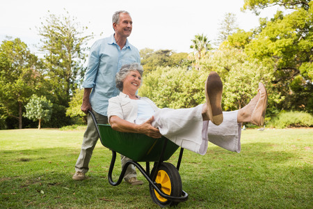 Smiling man pushing his wife in a wheelbarrow having fun outsideの写真素材