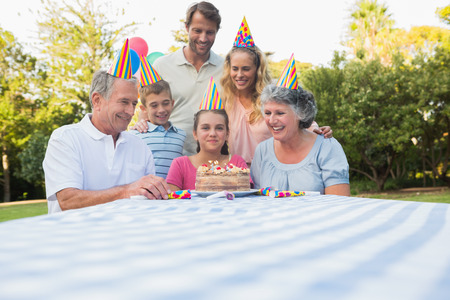 Happy extended family celebrating little girls birthday outside at picnic table
