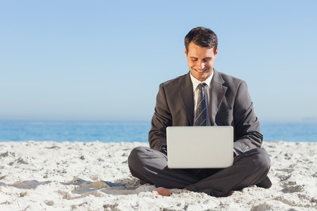 Young businessman with legs crossed typing on his laptop on the beachの写真素材