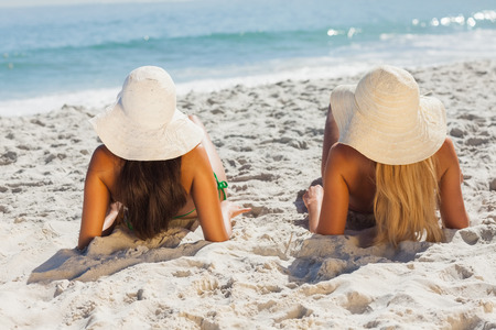 Attractive blonde and brunette in bikinis lying on the sand looking at the seaの写真素材