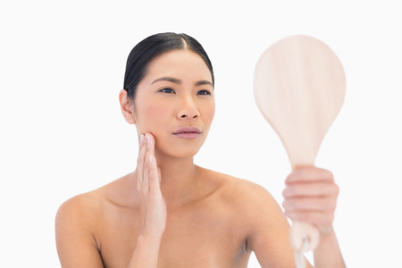 Natural dark haired model holding mirror touching her cheek on white backgroundの写真素材