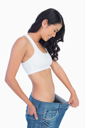 Cheerful woman holding her too big jeans on white backgroundの写真素材