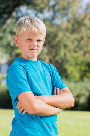 Young boy looking angry with crossed arms in the park looking at cameraの写真素材