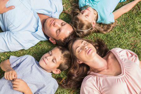 Family lying on the grass in a circle with closed eyes in the parkの写真素材