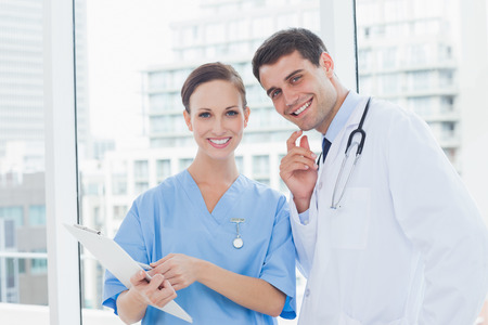 Cheerful surgeon and doctor posing while working together in bright officeの写真素材