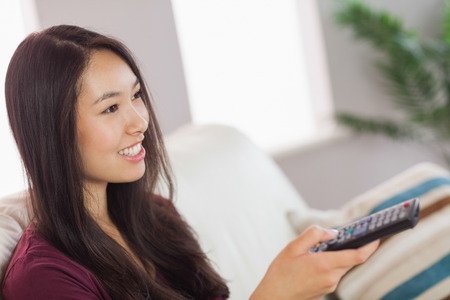Pretty asian girl watching tv at home in the living room