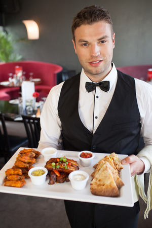Handsome waiter serving appetizing finger food platter in classy restaurantの写真素材