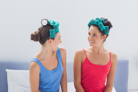 Girls wearing hair rollers sitting in bed at sleepoverの写真素材