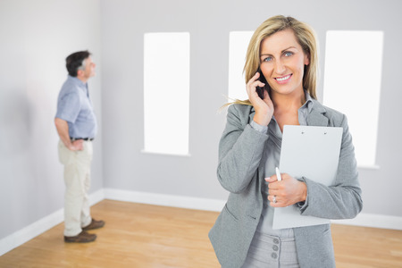 Happy realtor calling someone with her mobile phone in empty house with potential buyer smiling at cameraの写真素材