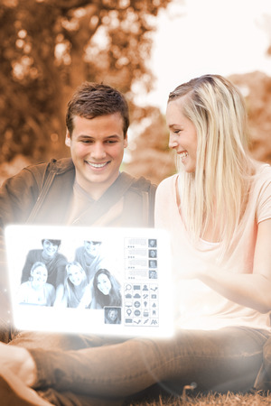 Happy young couple watching photos on digital interface in bright parkの写真素材