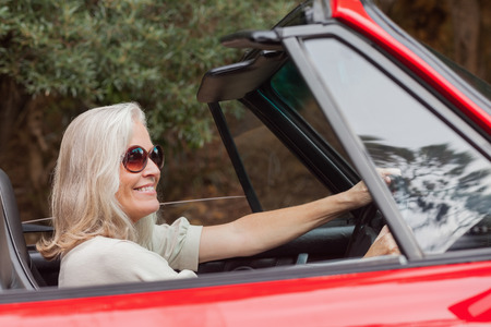 Happy mature woman with sunglasses driving red convertible on sunny day