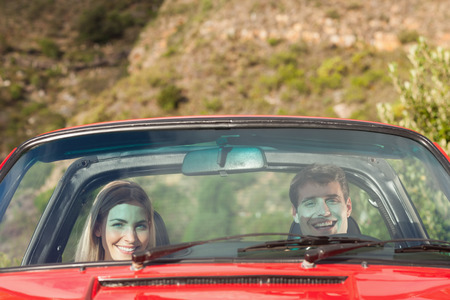 Front view of smiling couple in red cabriolet on a sunny day