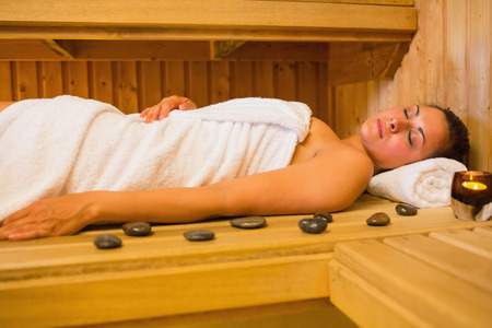 Peaceful brunette woman lying in a sauna with pebbles and candleの写真素材