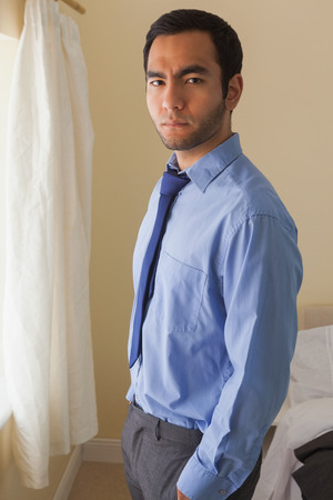 Angry man looking at camera standing in front of a window in a bedroom at homeの写真素材