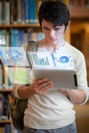 Serious handsome student working on his futuristic tablet pc in university library