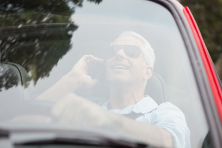 Smiling handsome man in red convertible having phone call while drivingの写真素材