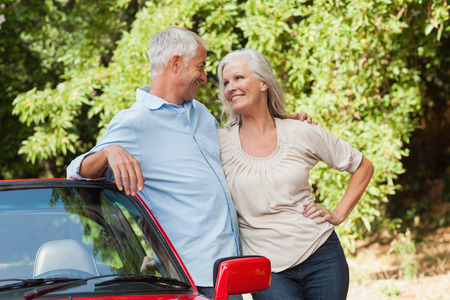 Smiling mature couple hugging by their red cabriolet on a sunny dayの写真素材