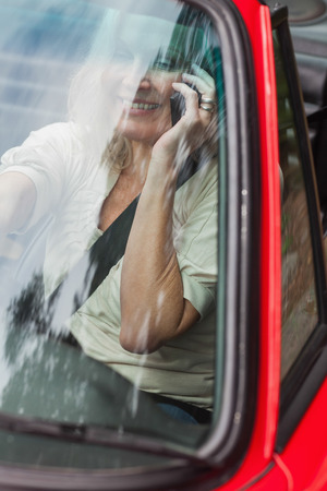 Smiling mature woman on the phone driving red cabriolet on sunny dayの写真素材