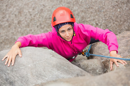 Smiling girl climbing up rock face looking at cameraの写真素材