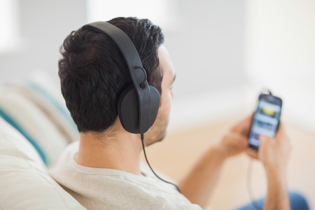 Handsome man listening to music on his smartphone sitting on cosy sofa