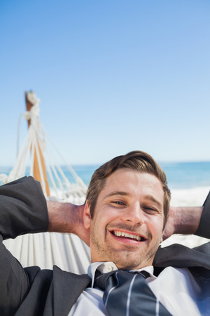 Smiling businessman relaxing in hammock looking at camera on sunny dayの写真素材
