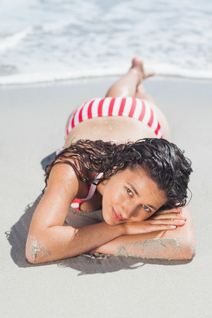Brunette woman lying down on beach looking at camera on holidaysの写真素材