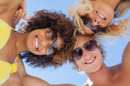 Low angle view of friends on beach wearing sunglasses smiling at cameraの写真素材