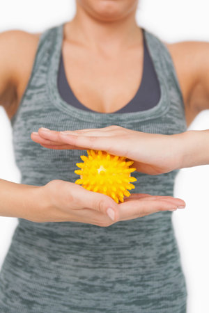Close up of young woman holding yellow massage ball between her hands on white screenの写真素材