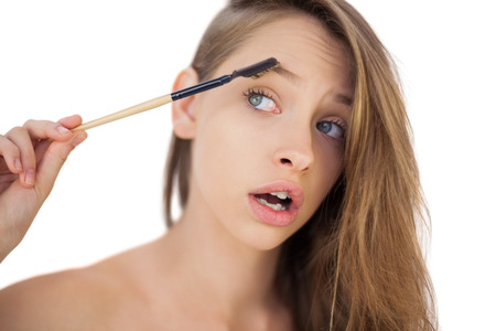Puzzled brunette model brushing her eyebrows on white background