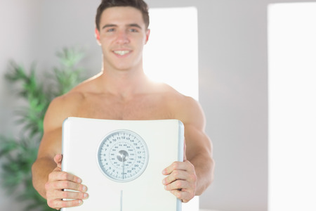 Confident cheerful handsome man showing scales in bright living roomの写真素材