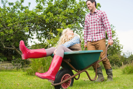 Cheerful man pushing his laughing girlfriend in a wheelbarrow through the gardenの写真素材