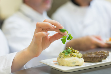 Female chef garnishing a plate with steak in commercial kitchenの写真素材