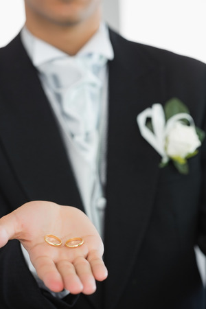 Young bridegroom showing wedding rings while wearing a suitの写真素材