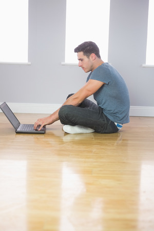 Focused handsome man using laptop sitting on floor in bright roomの写真素材