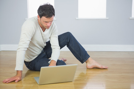 Casual good looking man sitting on floor using laptop in bright roomの写真素材