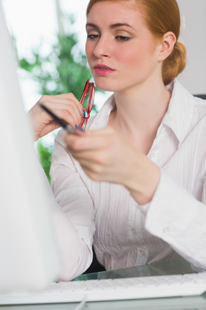 Serious businesswoman working at her desk holding glasses in her officeの写真素材