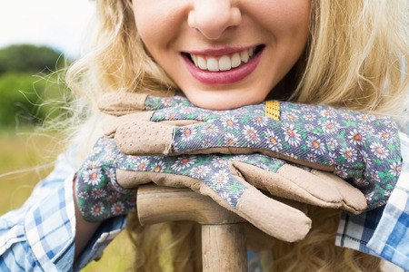Cheerful blonde woman leaning on a shovel wearing gardening gloves close upの写真素材