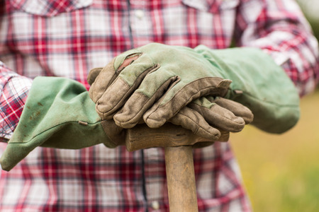 Farmer wearing check shirt leaning on a shovel standing outsideの写真素材