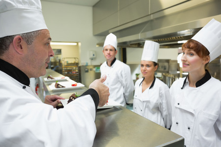 Head chef rating the plate of one of his apprentices in a kitchenの写真素材