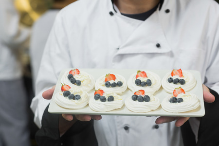Chef presenting plate of meringues in commercial kitchenの写真素材