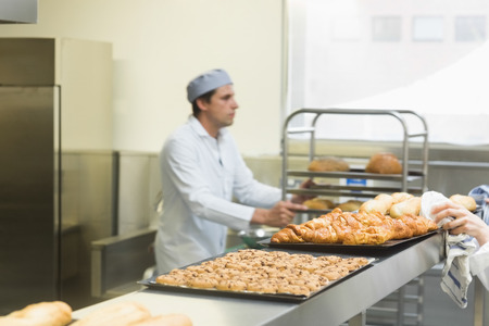 Young male baker working in a kitchen wearing a work coatの写真素材